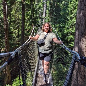 Photo of Allison Hubenig in the middle of a bridge in the forest smiling.